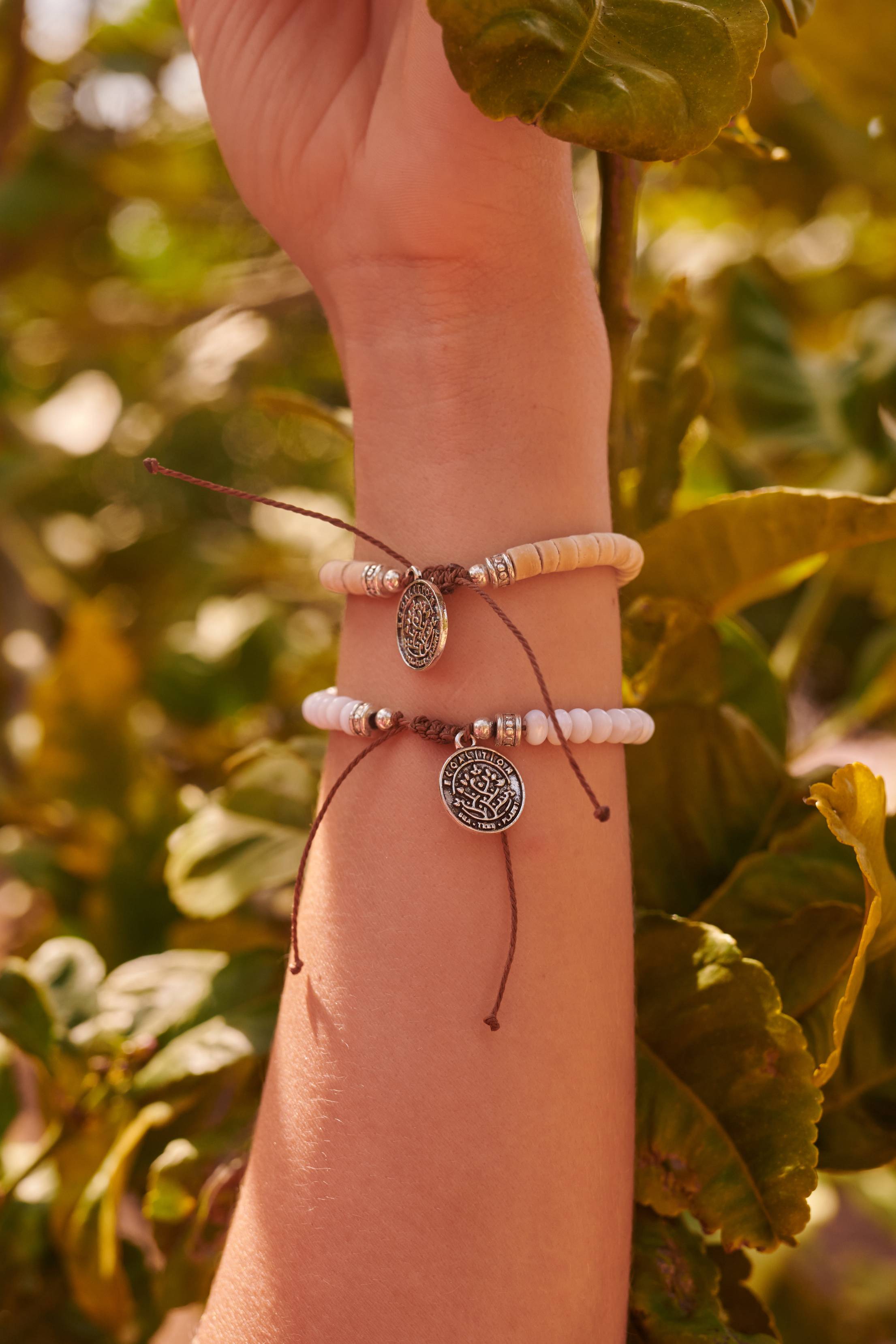 Woman's arm reaching up through leaves with two Ecoalition bracelets on her wrist